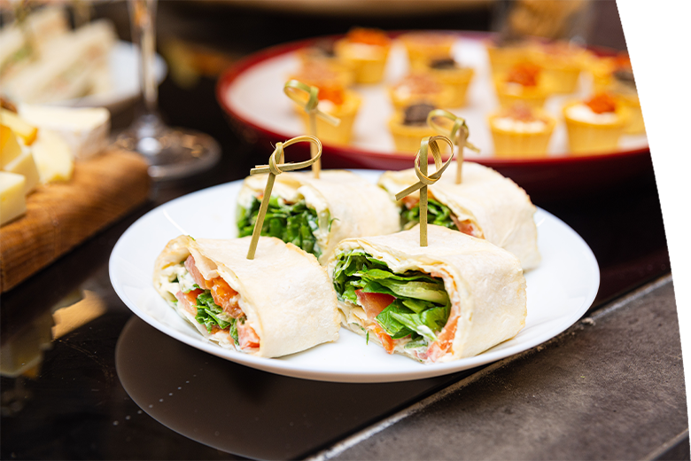 Plate of tortilla wrap pinwheels filled with lettuce, tomato, and cream cheese, secured with skewers, served as finger food